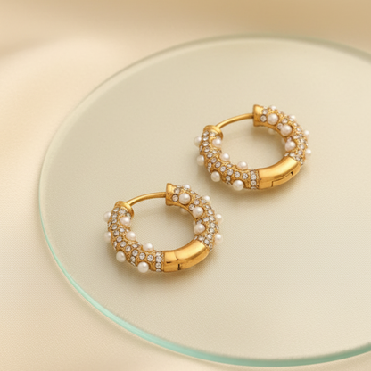 Gold hoop earrings with pearl accents on a beige surface